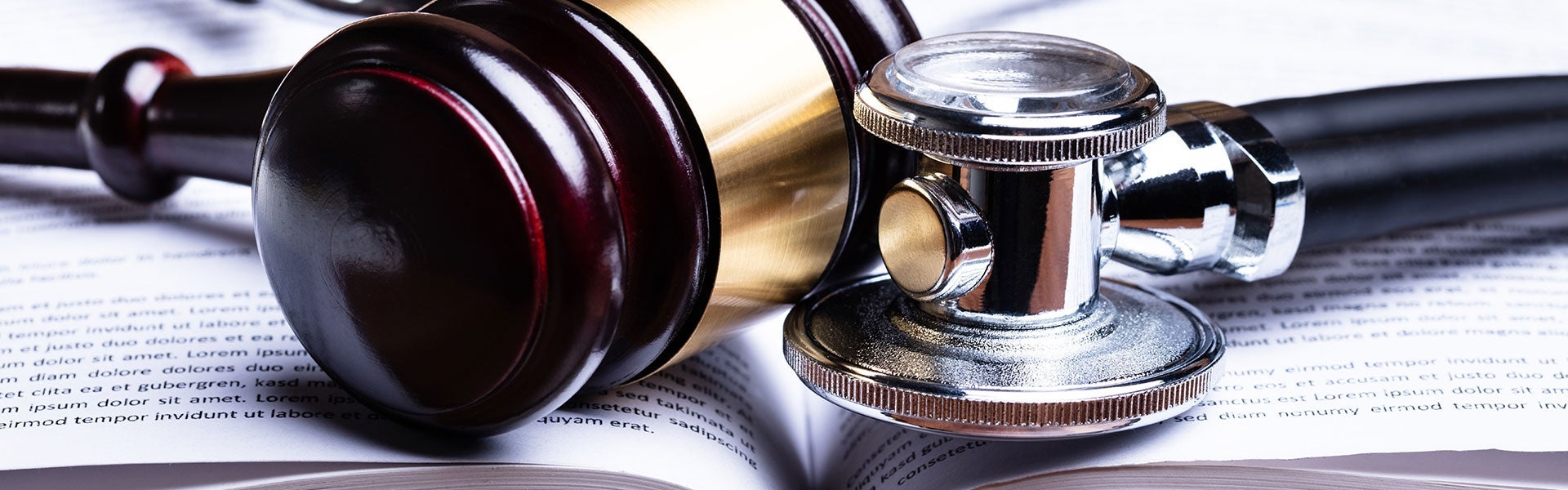 A silver stethoscope rests on an open book filled with text, suggesting a medical or legal context.