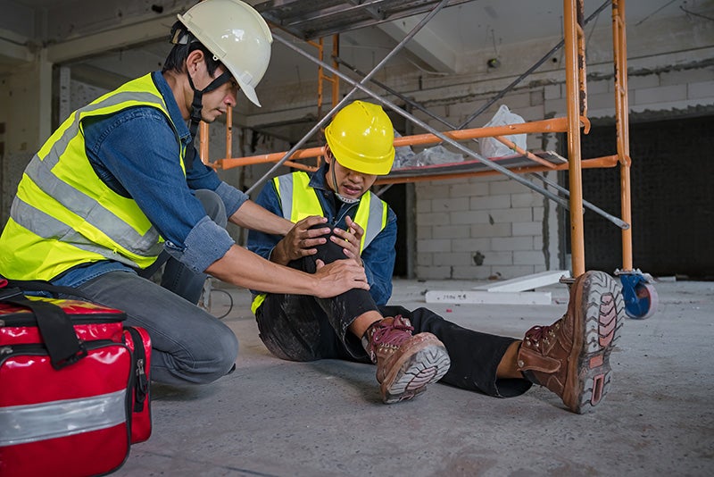 Construction worker assists a colleague who appears to be injured on a construction site.