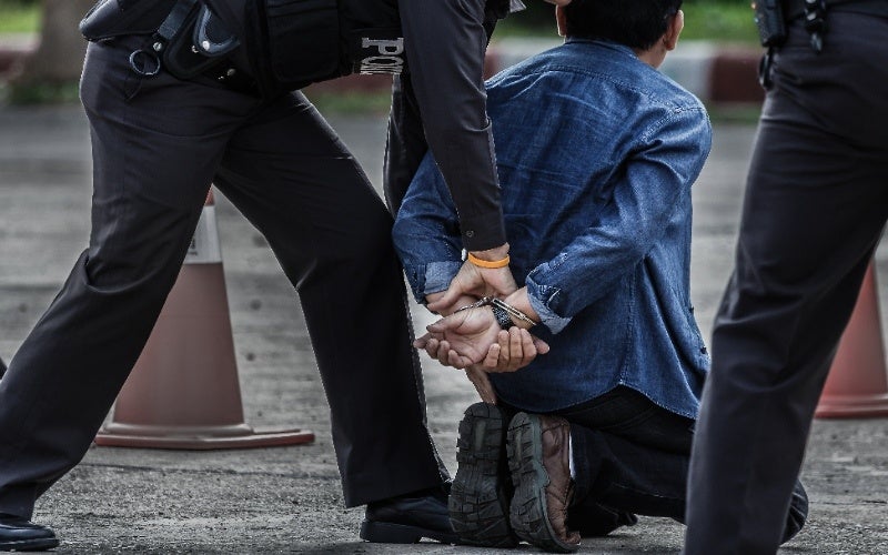 A police officer handcuffs a man who is kneeling on the ground.