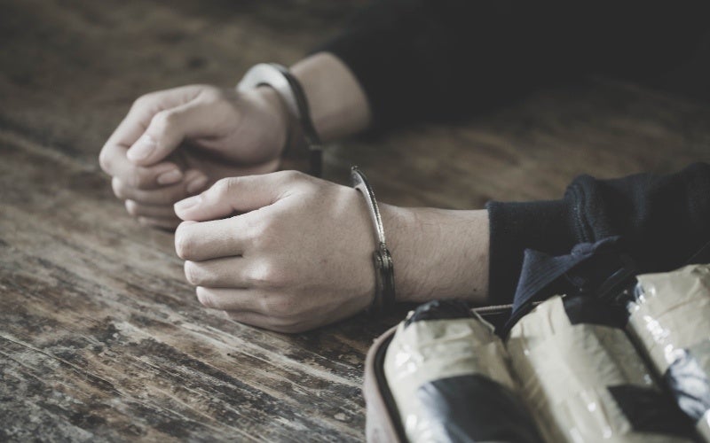 A person's hands are cuffed with metal restraints on a wooden surface.