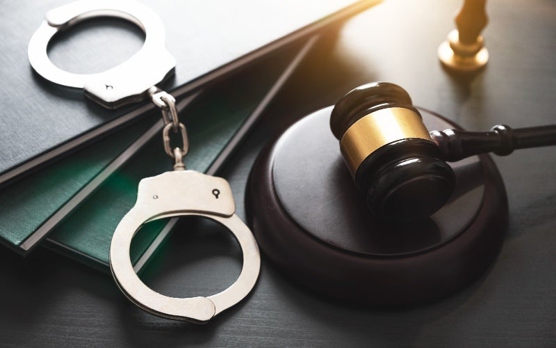 Handcuffs and a gavel rest on top of law books, symbolizing justice and legal authority.