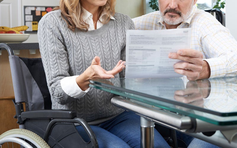 An older couple sits at a table reviewing documents, with the woman in a wheelchair.
