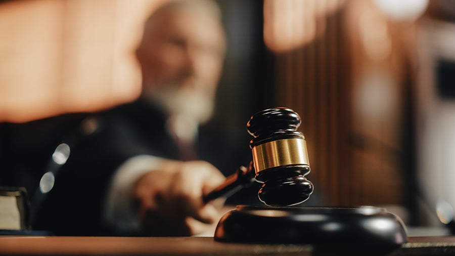A wooden gavel rests on a table, poised to strike, suggesting a courtroom setting.