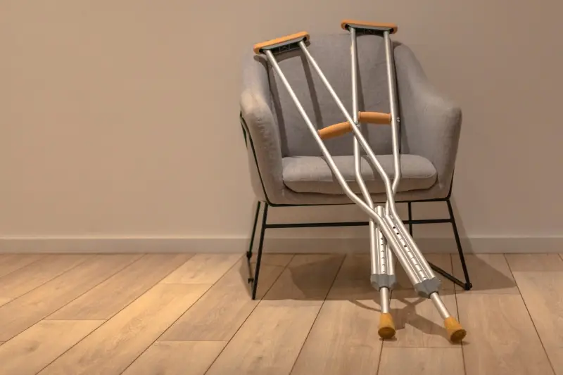 A pair of silver crutches rest crossed on a gray upholstered armchair.