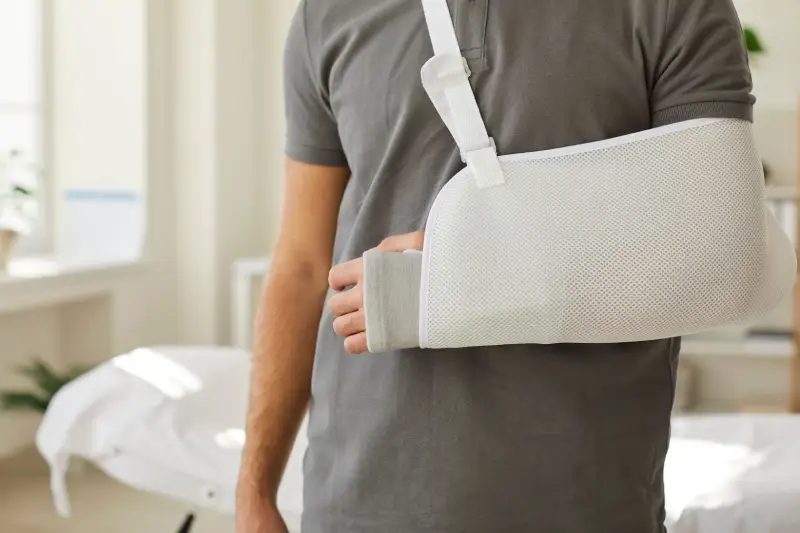 A man wearing a gray shirt has a white arm sling on his left arm.