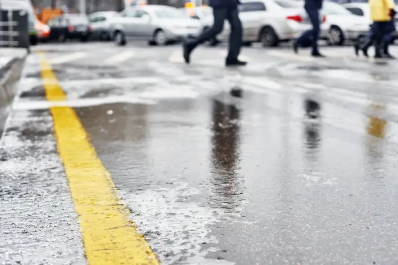 A person runs across a wet crosswalk between parked cars on a rainy day.