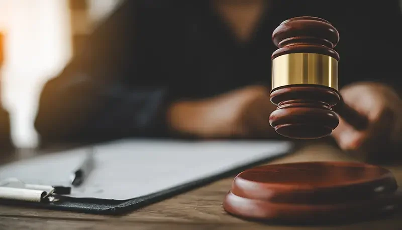 A wooden gavel suspended above a legal pad and pen, suggesting a courtroom setting.