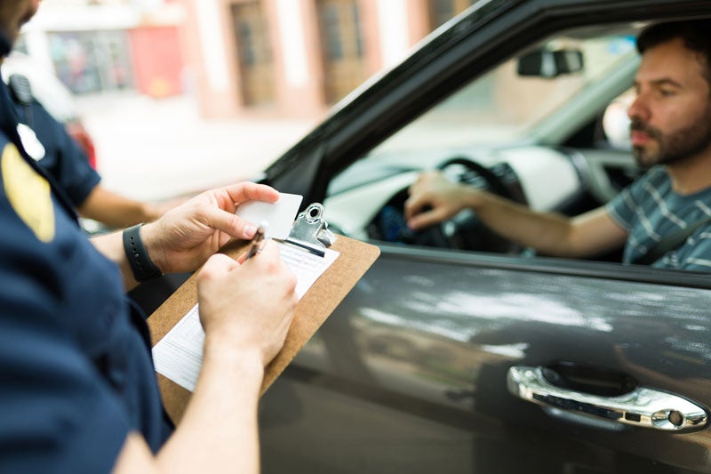 A police officer hands a driver's license to a man inside a car during a traffic stop.
